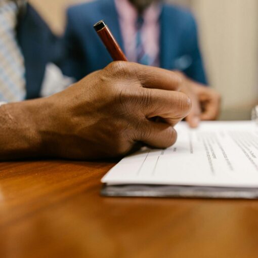 Close-up of an adult signing a legal document with a pen in an office.